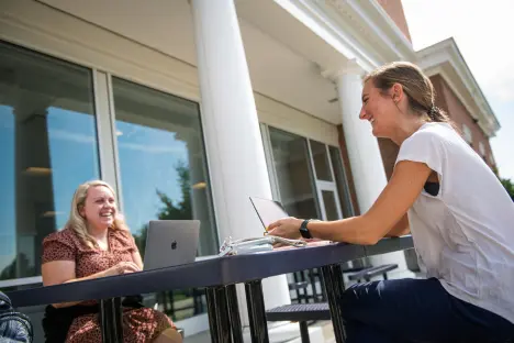 Photo of two students using computers outdoors